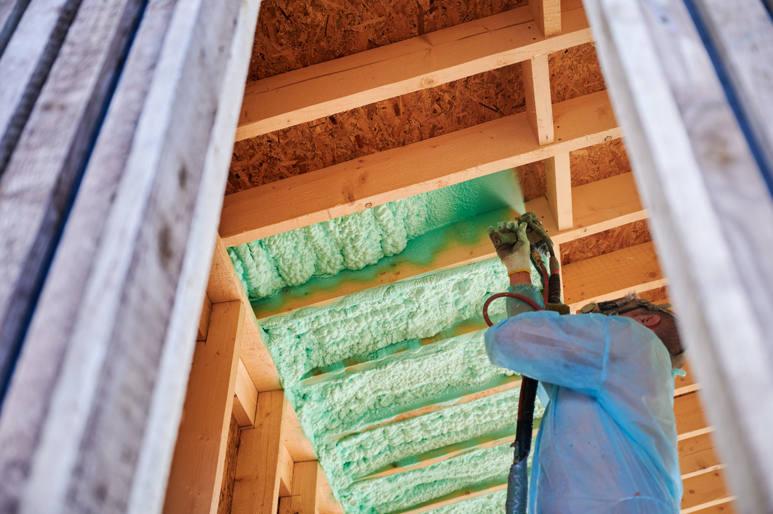 Worker spraying spray foam insulation around wooden frame house.